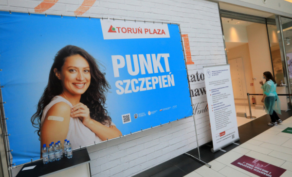 Na zdjęciu baner z uśmiechniętą kobietą i napisem Punkt Szczepień Toruń Plaza