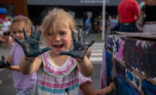 Na zdjęciu: usmiechnięta dziewczynka pokazuje dłonie pomalowane farbami