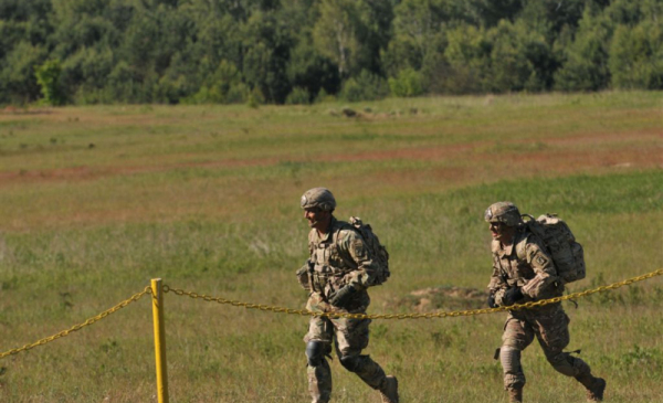 Na zdjęciu widać dwóch żołnierzy biegnących z bronią po terenie poligonu