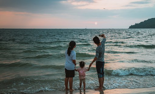 Na zdjęciu rodzina z dzieckiem stoi na plaży na tle morza