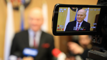 Prezydent Michał Zaleski w obiektywie kamery telewizyjnej przed mikrofonami dziennikarzy.