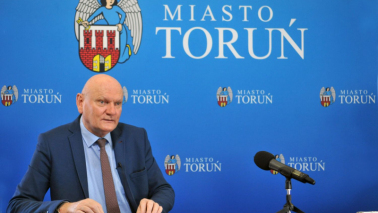 Prezydent Michał Zaleski podczas sesji Rady Miasta przeprowadzonej on-line siedzi na tleniebieskiej ścianki z herbem Torunia