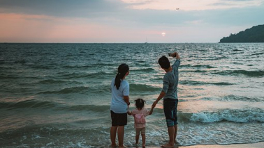 Na zdjęciu rodzina z dzieckiem stoi na plaży na tle morza