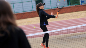 Na zdjęciu: dziewczynka stoi na korcie, trzyma rakietę do tenisa i odbija nią piłeczkę