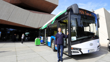 Na zdjęciu autobus elektryczny, przed nim stoi uśmiechnięty kierowca