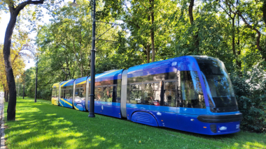 Na zdjęciu: niebieski tramwaj jedzie po torowisku porośniętym trawą