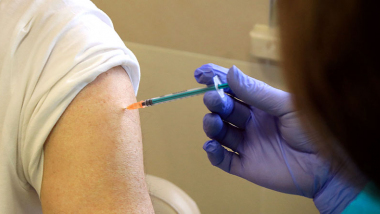 Reka w rękawiczce ze strzykawką dokonuje szczepienia w ramię pacjenta