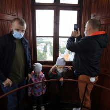 Na zdjęciu dwóch mężczyzn i dwoje dzieci stoją przy oknie w wieży ciśnień, jeden z mężczyzn robi zdjęcie telefonem
