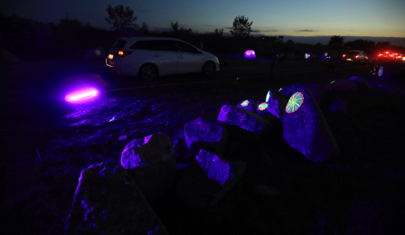 Na zdjęciu widać drobne podświetlone elementy umieszczone na kamieniach, w tle widoczny jest przejeżdżający samochód