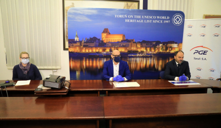 Zastępca prezydenta Zbigniew Rasielewski i Adam Banaszak, wiceprezes PGE Toruń oraz osoba prowadząca podczas konferencji prasowej, w tle ścianka z nocną panoramą Torunia