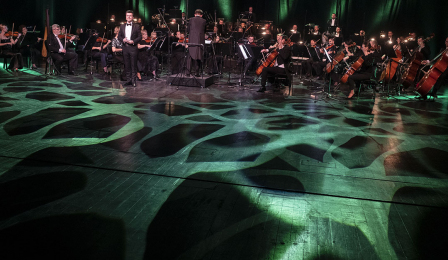 Toruńska Orkiestra Symfoniczka podczas koncertu noworocznego, na pierwszym planie światł oświetlają scenę