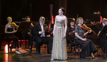 Sopranistka Aleksandra Borkiewicz ubrana w długą srebrną suknię śpiewa podczas koncertu