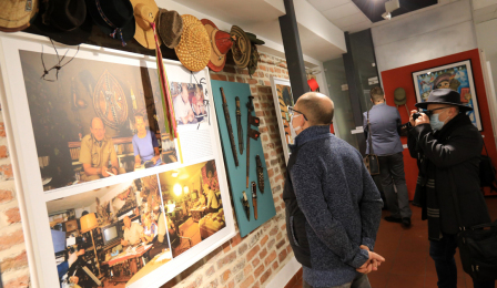 Dwóch mężczyzn ogląda eksponaty na wystawie poświęconej Tony'emu Halikowi, jeden z nich robi zdjęcie