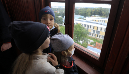 Na zdjęciu: troje dzieci patrzy przez okno w wieży ciśnień