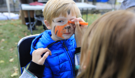 Na zdjęciu: podczas pikniku jest malowanie buzi dzieci - chłopiec ma twarz malowaną na pomarańczowo (tygrys) 