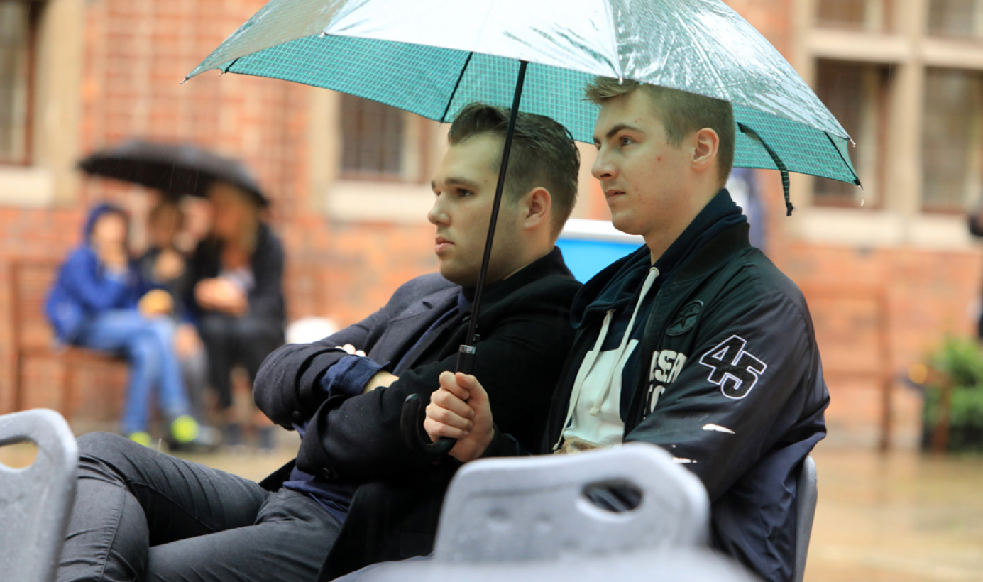 widzowie pod parasolami słuchają aktorów